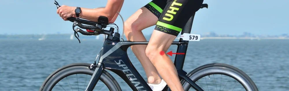 Ciclista numa bicicleta de contrarrelógio com indicação de dor na parte de trás do joelho