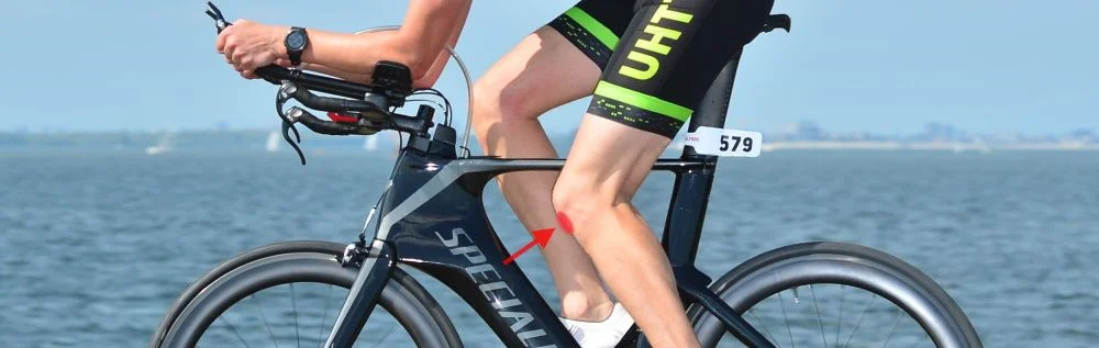 Ciclista numa bicicleta de contrarrelógio com indicação de dor na frente do joelho ao pedalar