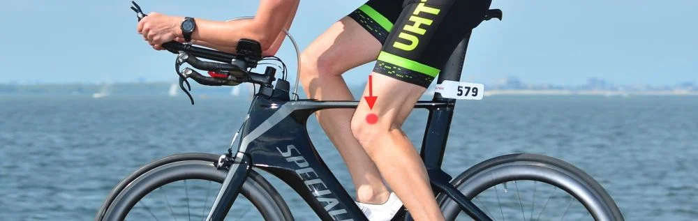 Ciclista numa bicicleta de contrarrelógio com indicação de dor no exterior do joelho ao pedalar